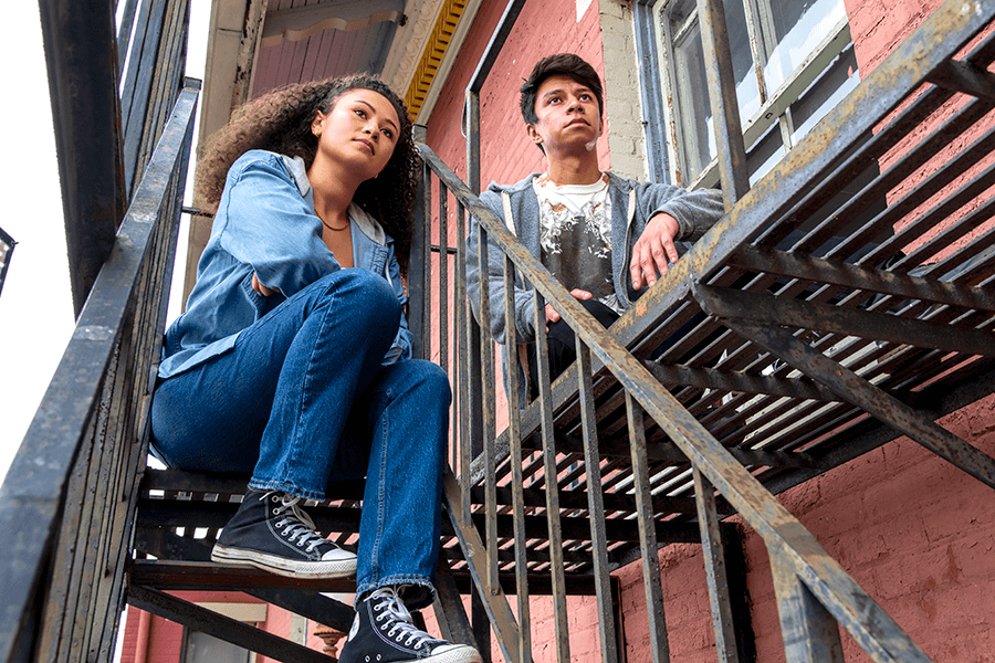 Young mixed-race couple sitting on fire escape of a red brick building.