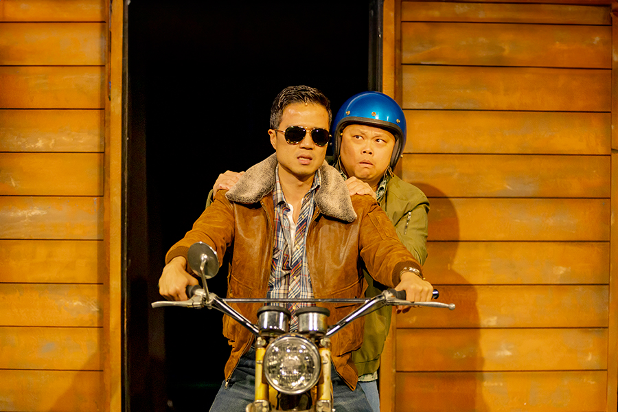 Young asian couple on a laden motorcycle moving quickly with an open cloudy sky.